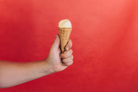 Man holds an ice cream in his hand on a red backgroundの写真素材