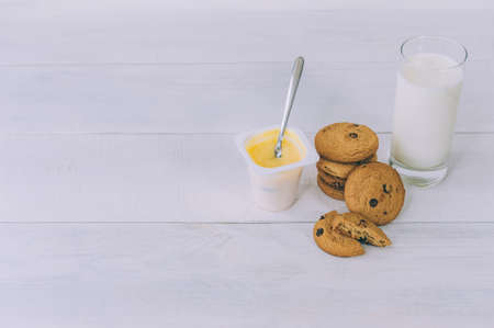 Oatmeal cookies with chocolate on a light background with a glass of milk and yogurtの写真素材
