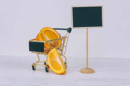 Fresh tropical oranges in a supermarket trolley and a plate on a light backgroundの写真素材