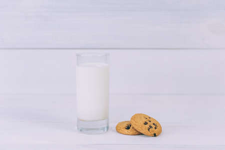 Oatmeal cookies with chocolate on a light background with a glass of milkの写真素材