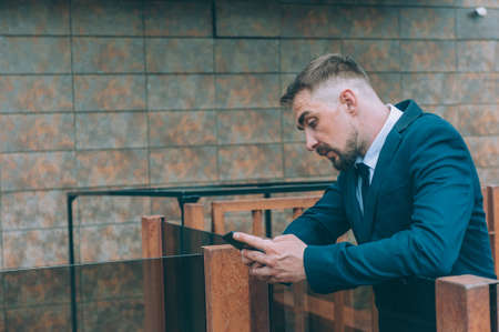 Businessman in a blue jacket with a smartphone in his hand on a wall background