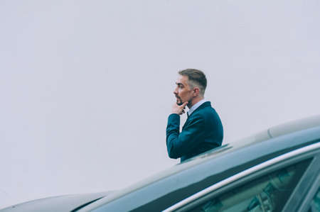 Businessman in a blue jacket on the background of the car