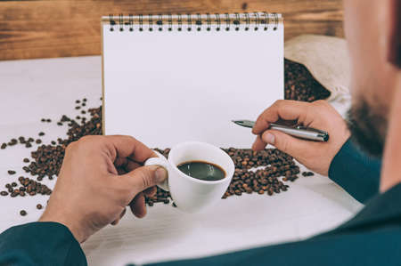The guy holds in his hands a coffee cup on a background of beans and a notebookの写真素材