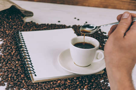 A man stirs coffee on a background of a notebook and beansの写真素材