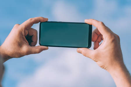 Mock-up smartphone in the hands of a person against the skyの写真素材