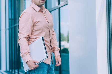 Businessman in a pink shirt with a Laptop in his hand stands against the backdrop of a modern...