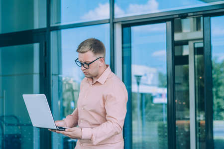 Businessman in a pink shirt with a Laptop in his hand stands against the backdrop of a modern...