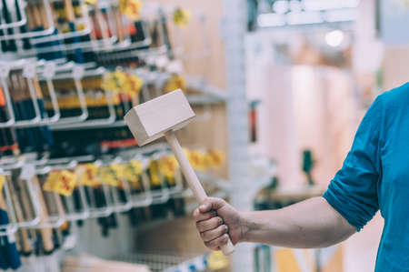 The buyer in the hardware store selects the goods. A man holds a wooden construction hammer in his handの写真素材