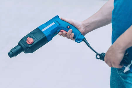 A man holds an electric drill in his hand for drilling. A buyer in a hardware store selects a...