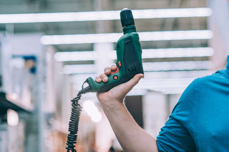 A man holds an electric drill in his hand for drilling. A buyer in a hardware store selects a...