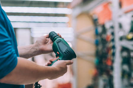 A man holds an electric drill in his hand for drilling. A buyer in a hardware store selects a productの写真素材