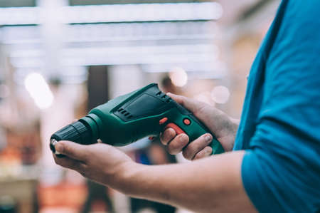 A man holds an electric drill in his hand for drilling. A buyer in a hardware store selects a...