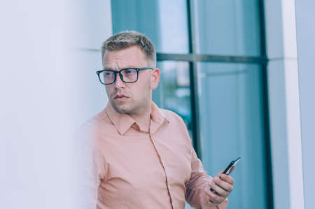 Businessman in a pink shirt with a smartphone in his hand stands against the backdrop of a modern...