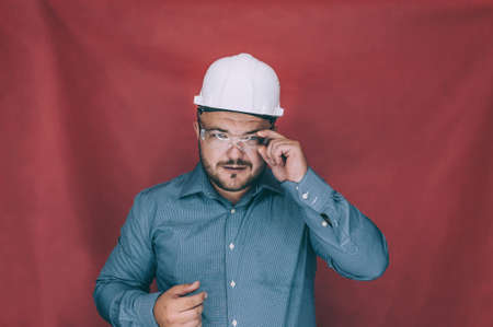 A man in safety glasses and a construction helmet on a red background