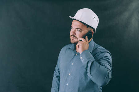 A man in a construction helmet talking on the phone on a dark background