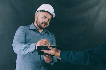 A man in a construction helmet signs a document on a dark backgroundの写真素材
