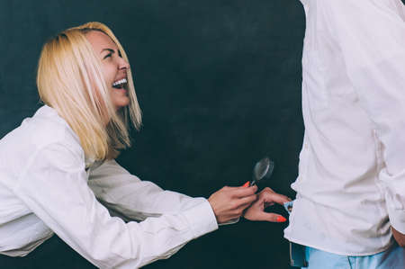 A woman with a magnifying glass in her hands checks male dignity with a guy