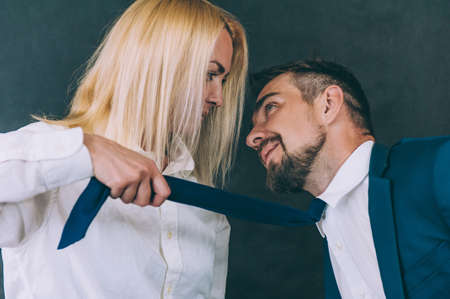 A girl pulls a businessman by a tie on a dark background