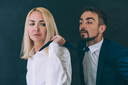A girl pulls a businessman by a tie on a dark background
