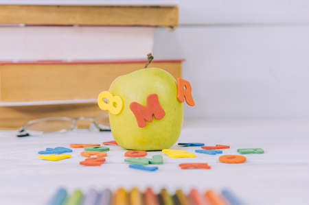 Concept Back to School. Green apple with colored letters on the background of books