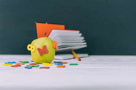 Concept Back to School. Green apple with colored letters and notepad background