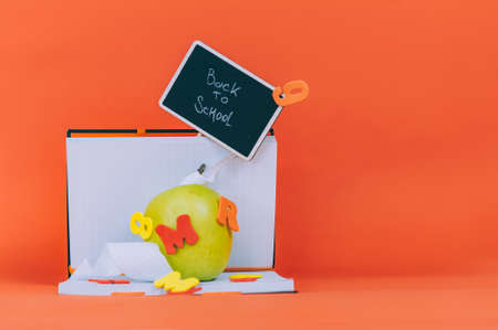 Concept Back to School. Green apple with colored letters and a notebook with a tablet on an orange backgroundの写真素材