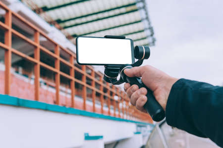 Blogger in the stadium shoots video on a smartphone with a manual camera stabilizerの写真素材