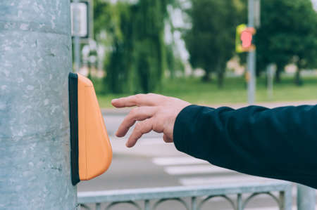 Man hand clicks on the traffic light button, against the background of a pedestrian crossing