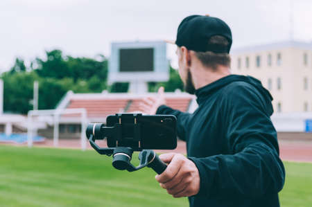 Blogger in the stadium shoots video on a smartphone with a manual camera stabilizer