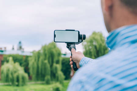 Blogger in nature shoots video on a smartphone with a manual camera stabilizerの写真素材