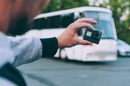 Blogger with an action camera in his hands, against the background of a busの写真素材
