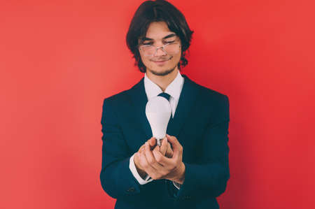 Businessman with a light bulb in his hands, on a red background. Concept on the topic of ideasの写真素材