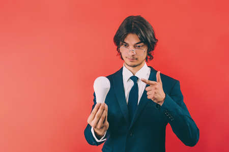 Businessman with a light bulb in his hands, on a red background. Concept on the topic of ideasの写真素材