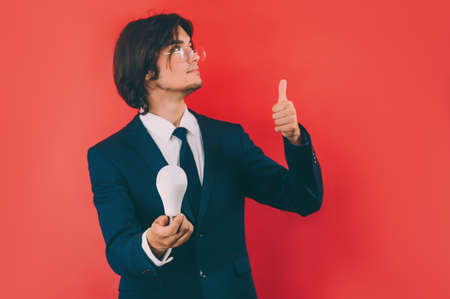 Businessman with a light bulb in his hands, on a red background. Concept on the topic of ideasの写真素材