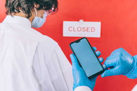 Two doctors with blue gloves, face masks and white coats check a blood test with a smartphone in their handsの写真素材