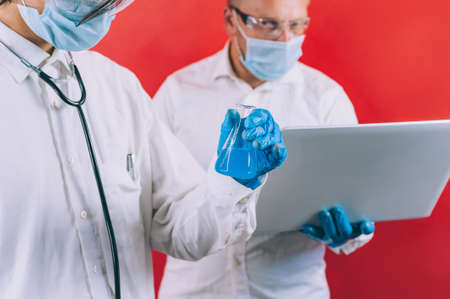 Two doctors with blue gloves in masks on the face with a laptop on a red backgroundの写真素材