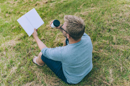 The guy with a cup of coffee reads a book outdoorsの写真素材