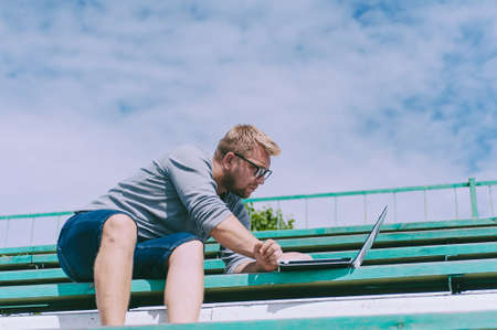 The guy works at a laptop on a bench outdoors against a background of grass