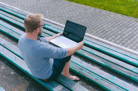 The guy works at a laptop on a bench outdoors against a background of grassの写真素材