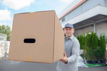 A man in a gray suit in his hands with a cardboard box against the background of the supermarket....