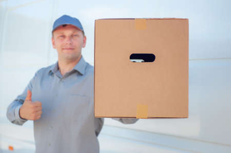 A man in a gray suit in his hands with a cardboard box against the background of the van. Concept on...