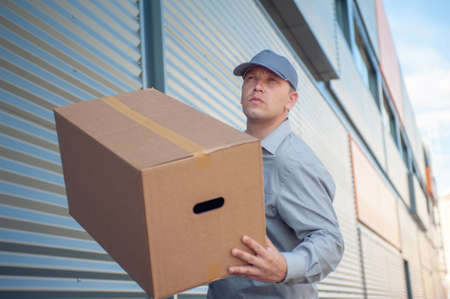 A man in a gray suit in his hands with a cardboard box against the background of the supermarket....