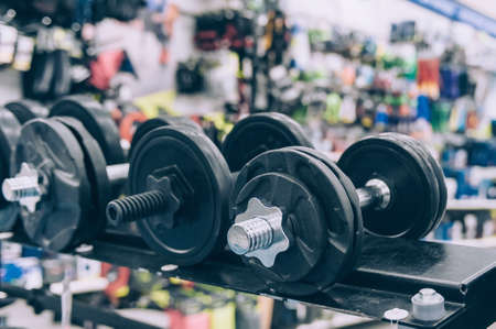 The guy holds a dumbbell in his hands at the sports store on the background of accessories for fitnessの写真素材