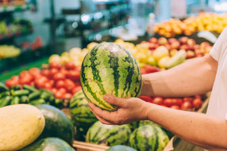 A man holds a watermelon in his hands in a supermarketの写真素材