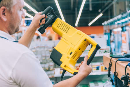 A man holds a puncher in his hands. Concept man selects a product in a hardware store