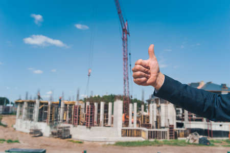 A hand with a finger shows the class on the background of a tower crane and building a houseの写真素材