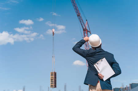 The chief in a jacket and a construction helmet with documents in his hands, against the background...