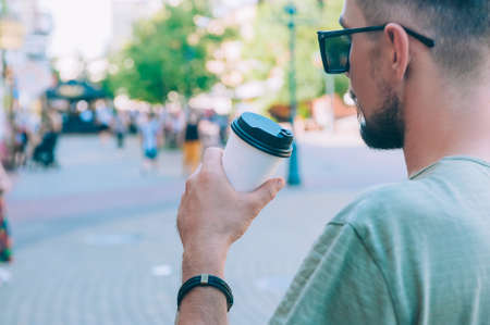 The guy drinks coffee in a plastic cup against the background of the city and peopleの写真素材