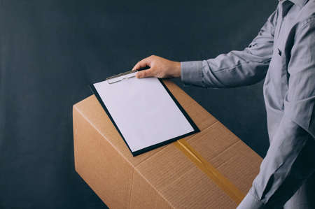 Guy with a cardboard box in his hands. Delivery service concept on dark backgroundの写真素材