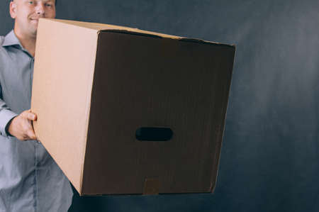 Guy with a cardboard box in his hands. Delivery service concept on dark backgroundの写真素材